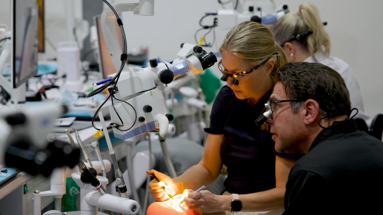 Two dental professionals at a simulation lab station, one working on a phantom head model while the other observes